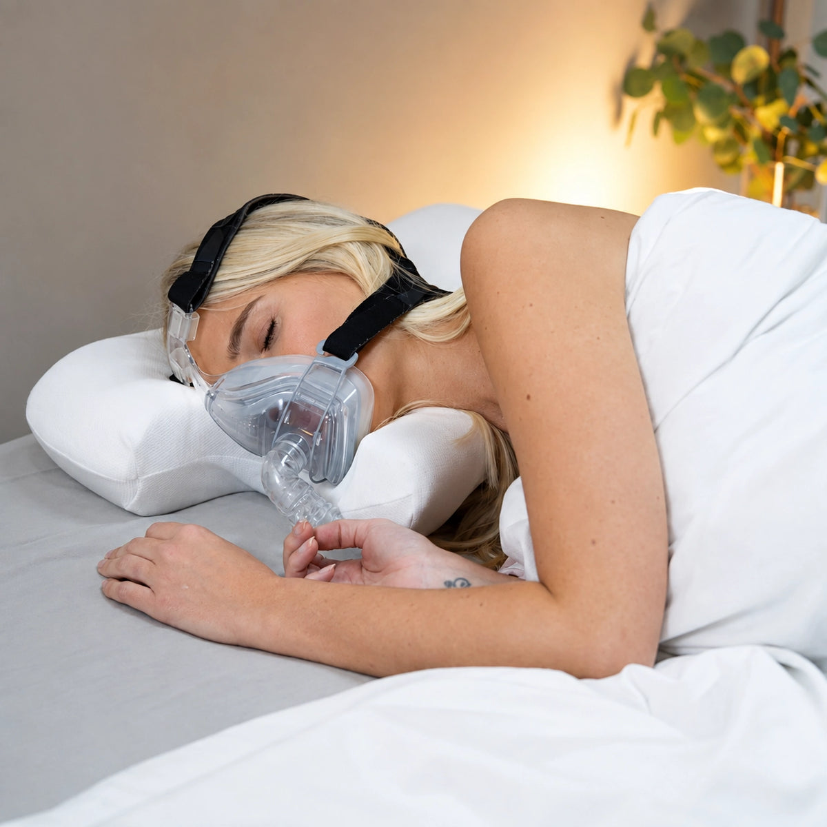 Woman side sleeping in a nasal CPAP mask with the mask resting in the pillow's side cut-out